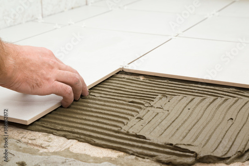 Φωτογραφία Worker hands gluing white ceramic tiles on floor. Closeup.