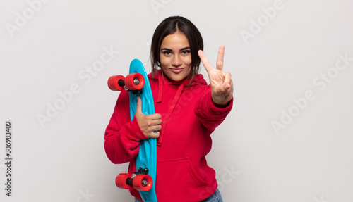 young hispanic woman smiling and looking friendly, showing number two or second with hand forward, counting down photo