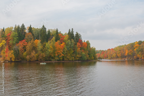 View to Perse river in Koknese from Koknese nature trail in autumn. Colorful red and yellow trees on the other river bank. Boat with fishermen in the river