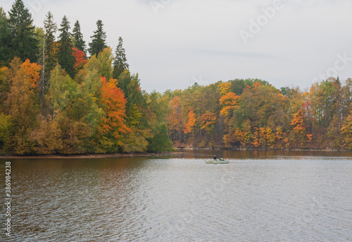 View to the boat with fishermen fishing in the Perse river in Koknese. Colorful red and yellow trees on the other river bank. 