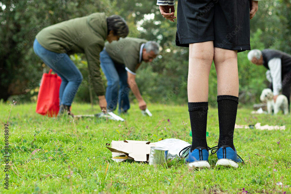 Boy standing watches adults pick up trash in a forest Boy standing watches adults pick up trash in a forest