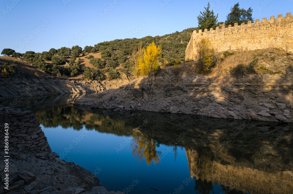 Autumnal landscape with the Lozoya river passing by the walls of Buitrago de Lozoya and the trees with autumn colors, Madrid, Spain