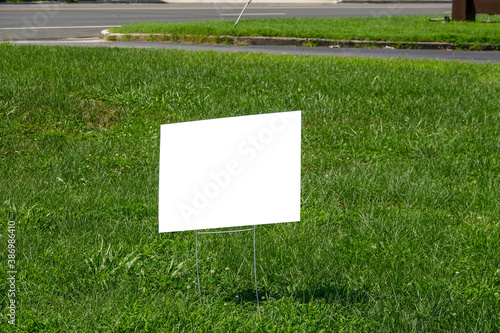 Blank white lawn sign on metal spikes on green grass near a sidewalk and street