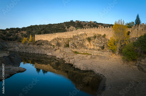 Autumnal landscape with the Lozoya river passing by the walls of Buitrago de Lozoya and the trees with autumn colors, Madrid, Spain