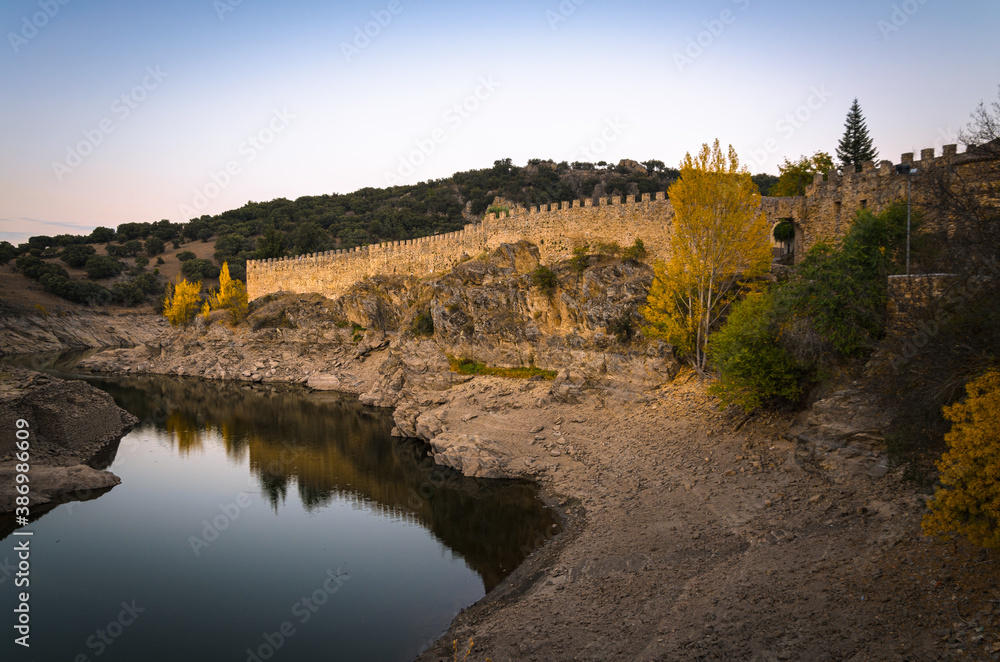 Walls of Buitrago de Lozoya reflected in the waters of Lozoya river at sunset, Madrid, Spain