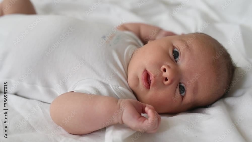 A newborn boy lies on a large bed of parents in the bedroom at home, moves his arms and looks at the camera
A newborn boy lies on a large bed of parents in the bedroom at home, moves his arms and looks at the camera