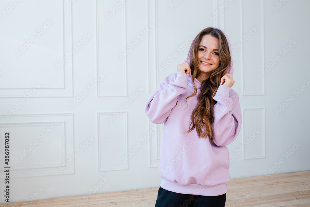 Happy girl fitness trainer in pink hoodie overalls stands against the background of a white wall in a fitness studio Happy girl fitness trainer in pink hoodie overalls stands against the background of a white wall in a fitness studio