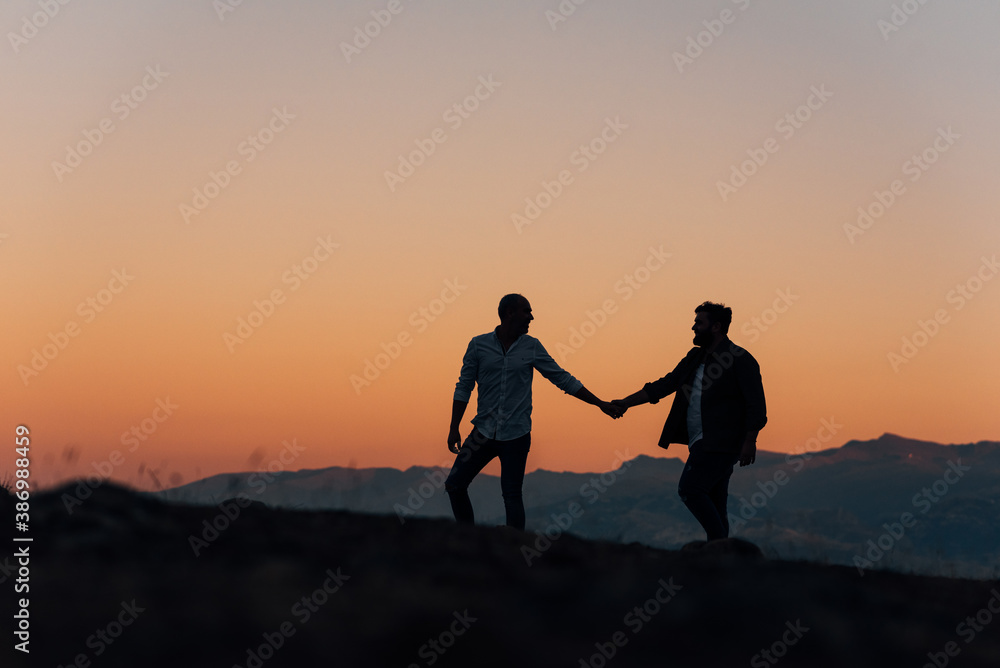 Silhouette of a gay couple holding hands walking at sunset.