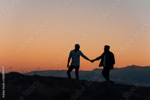 Silhouette of a gay couple holding hands walking at sunset.