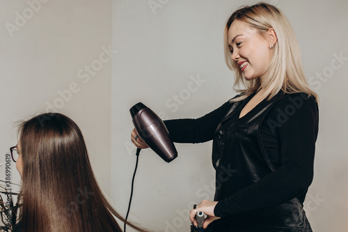A female hairdresser of European appearance works with the hair of a model. Home beauty salon. Barbershop. Healthy strong hair.