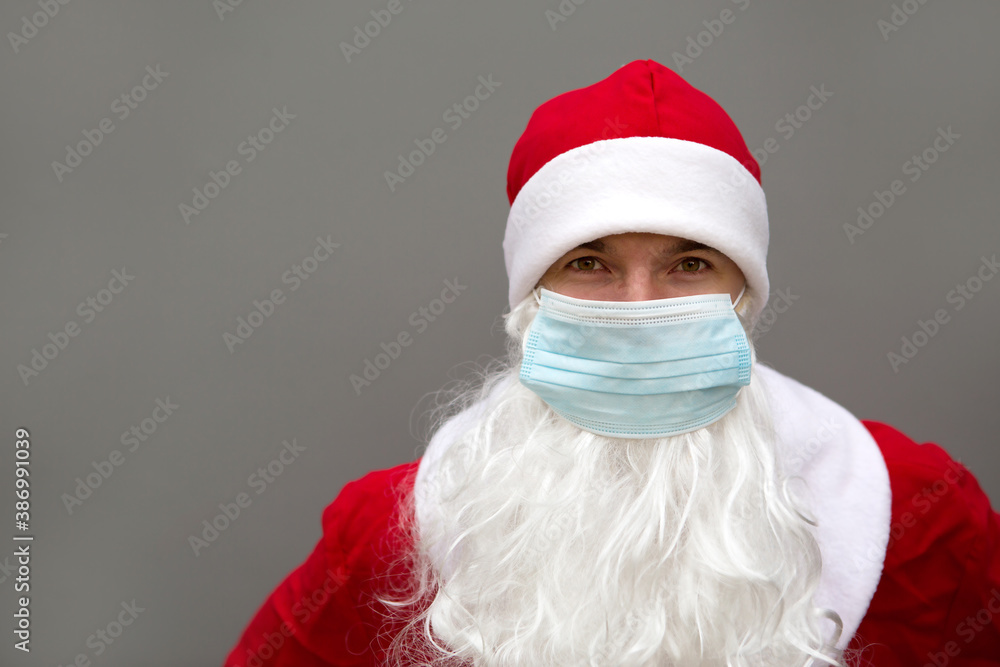 Santa Claus with white beard in red coat in a medical mask. Christmas in the coronavirus pandemic, seasonal diseases, SARS and pneumonia in the holidays. Protection from viruses in the new year. Gray Santa Claus with white beard in red coat in a medical mask. Christmas in the coronavirus pandemic, seasonal diseases, SARS and pneumonia in the holidays. Protection from viruses in the new year. Gray
