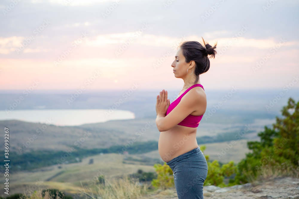 young pregnant woman does yoga outdoors. Yoga at sunset