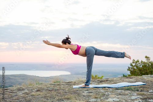 young pregnant woman does yoga outdoors. Yoga at sunset