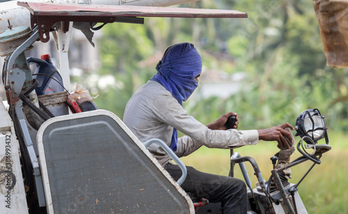 Face covered man in hot conditions as he operates combine harvester in the paddy field.