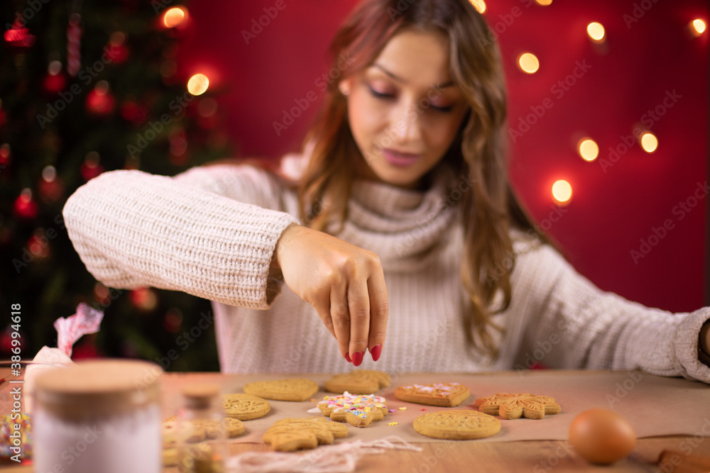 Portrait of Pretty brunette girl decorating christmas cookies with Christmas tree and red Xmas decoration on backdrop. handmade Mindful Gifting.