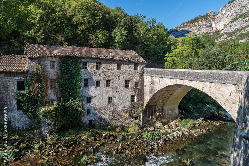 Old stone house on the edge of a river and a bridge in the Alps in France