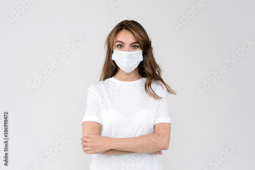 Studio portrait of young woman wearing a face mask, looking at camera, with crossed arms on her chesrt, close up, isolated on gray background. Flu epidemic. City air pollution concept © Iryna