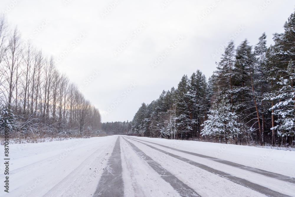 Patterns on the winter highway in the form of four straight lines. Snowy road on the background of snow-covered forest. Winter landscape. Patterns on the winter highway in the form of four straight lines. Snowy road on the background of snow-covered forest. Winter landscape.