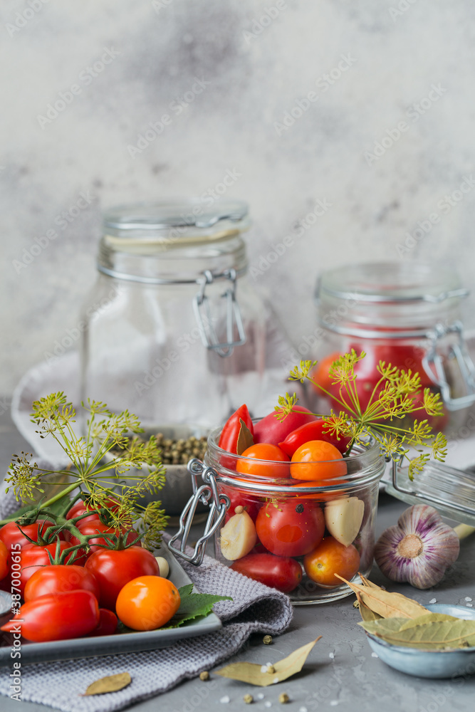 Preserving fresh and pickled tomatoes, seasonings and garlic on grey concrete table. Healthy fermented food. Home canned vegetables. Preserving fresh and pickled tomatoes, seasonings and garlic on grey concrete table. Healthy fermented food. Home canned vegetables.