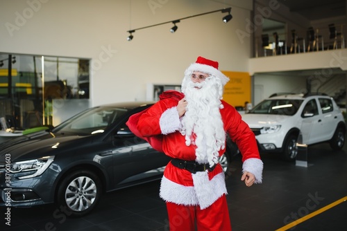 New car as a Christmas present. Santa Claus in the car showroom near a new car.