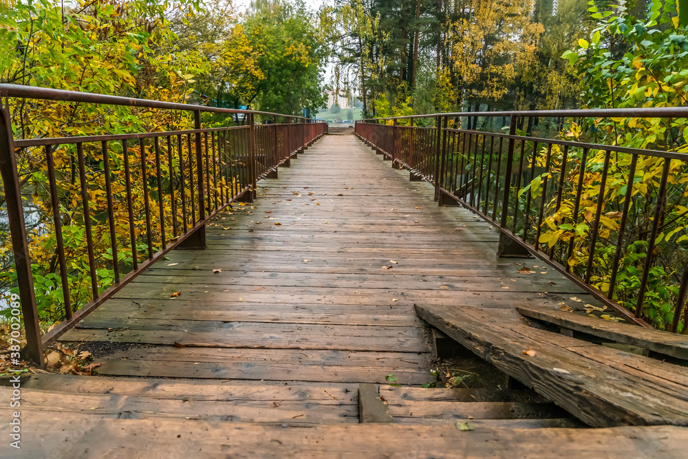 Beautiful wooden bridge with metal handrails across the river with beautiful, bright autumn trees on a rainy day close-up Beautiful wooden bridge with metal handrails across the river with beautiful, bright autumn trees on a rainy day close-up
