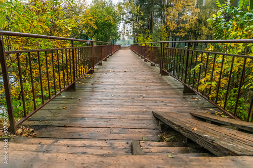Beautiful wooden bridge with metal handrails across the river with beautiful  bright autumn trees on a rainy day close-up