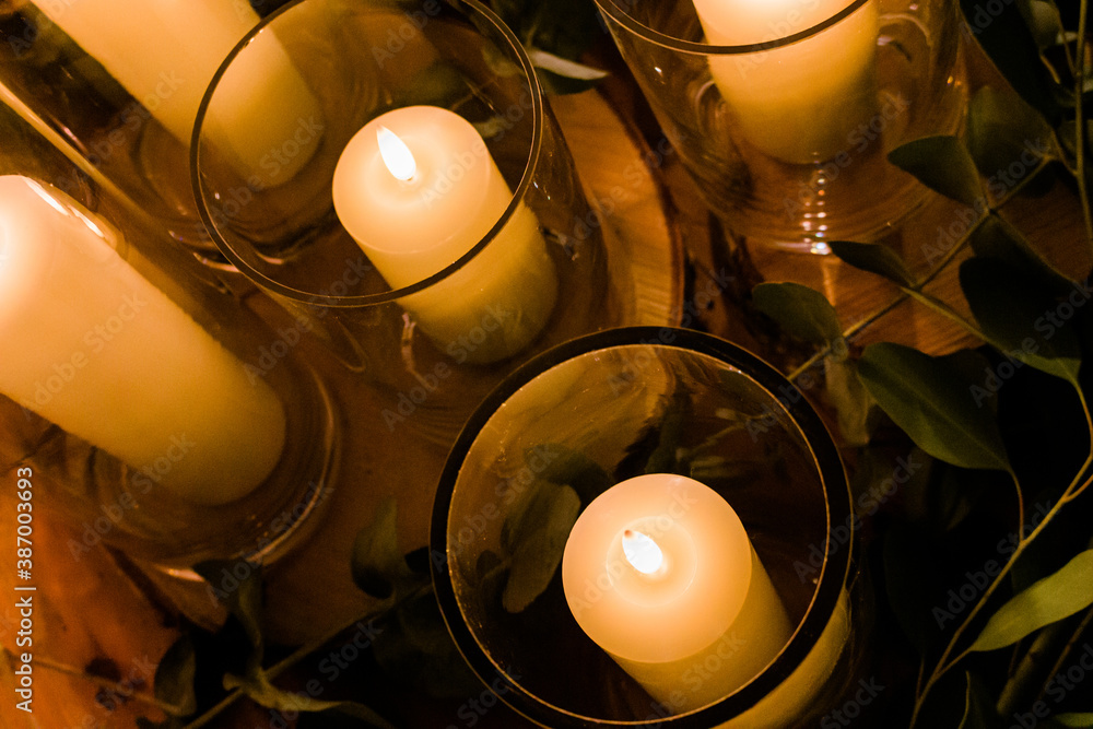 Romantic wedding display of wax candles glowing with small flames in glass vases centrepieces