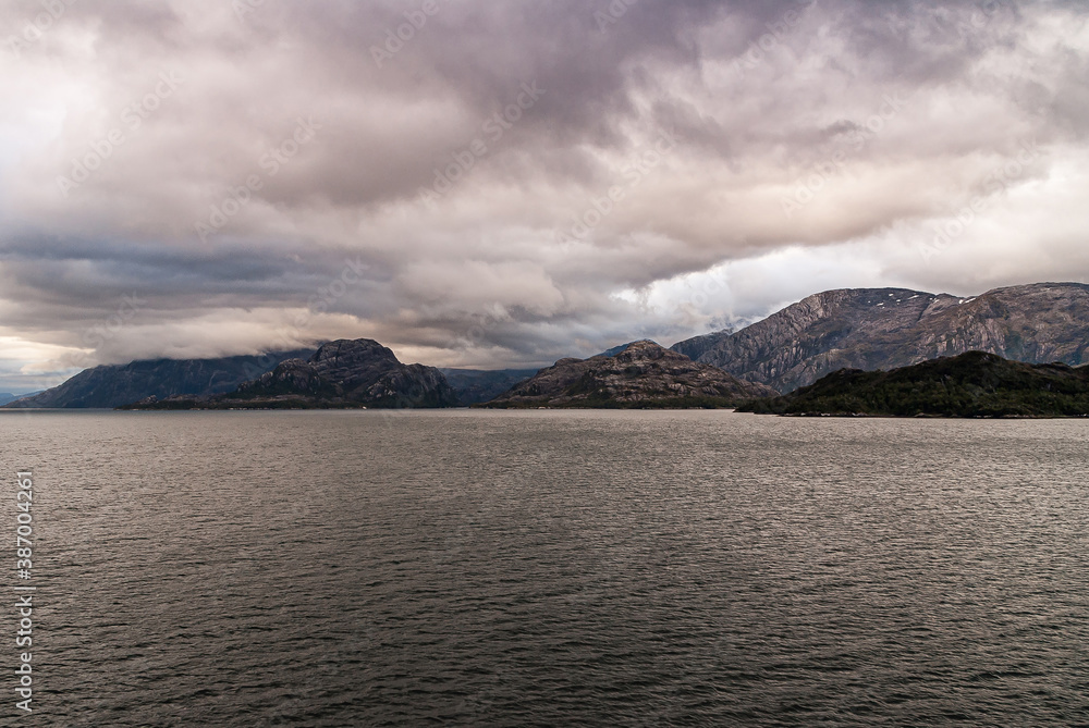 Sarmiento Channel, Chile - December 11, 2008: Amalia Glacier and Fjord. Thick brown cloudscape above and covering top of brown rocky mountains at entrance from dark-gray Pacific Ocean water.