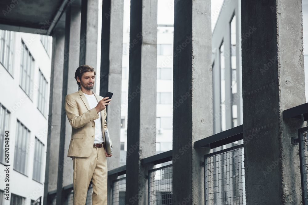 Young businessman standing outside with mobile and laptop