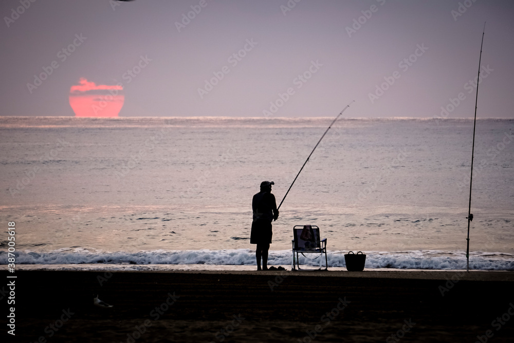 man fishing in the sea with the sun in the background