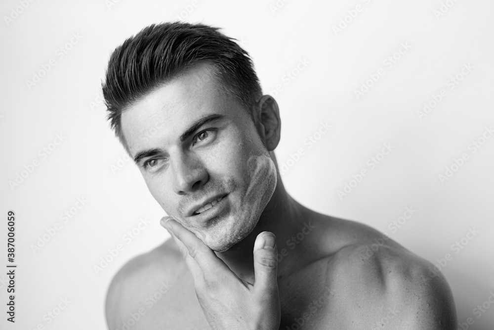 Fototapeta premium Muscular sexy model sports young man. Black and white portrait of beautiful smiling healthy guy applying foam for washing on his face. Facial skincare routine.