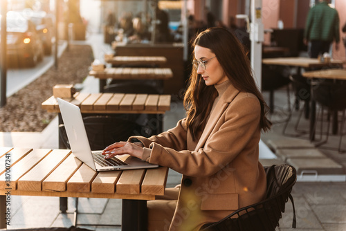 Close-up of young professional business woman using her laptop outside while working at modern business center, modern buildings in the background.