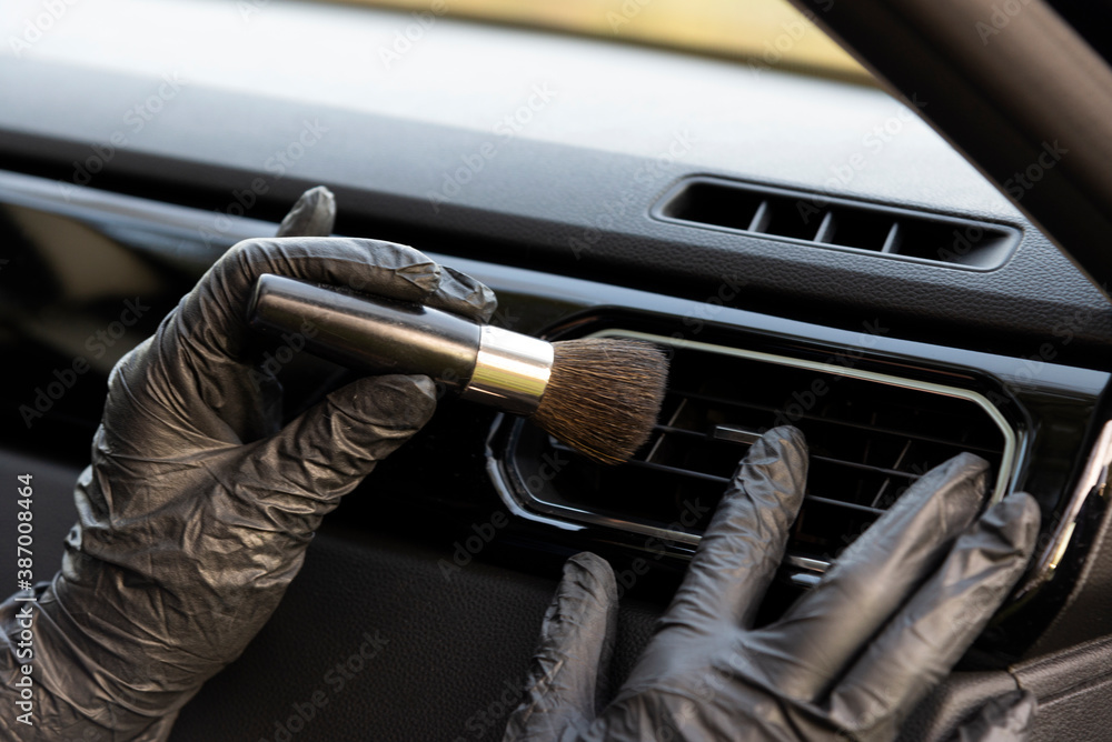 Obraz premium Worker cleaning automobile air conditioner vent grill with brush, closeup. Car wash service