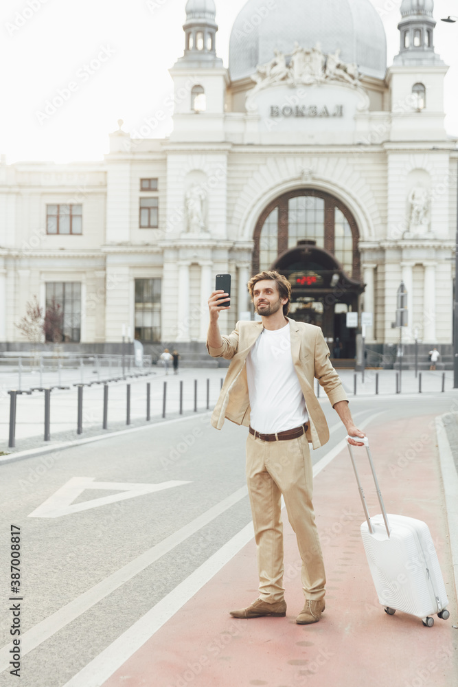Businessman with suitcase taking pictures on smartphone