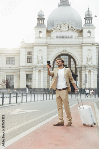 Smiling man with luggage using smartphone outdoors