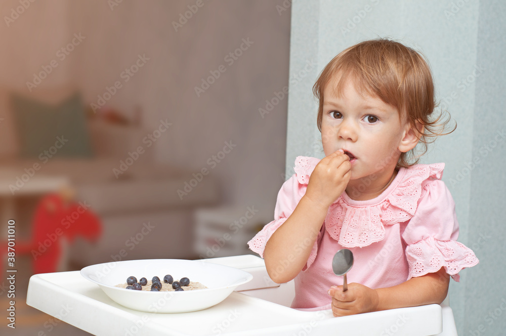 Happy, smiling child eating oatmeal with berries. The concept of a healthy breakfast for children, porridge with blueberries on baby chair Happy, smiling child eating oatmeal with berries. The concept of a healthy breakfast for children, porridge with blueberries on baby chair