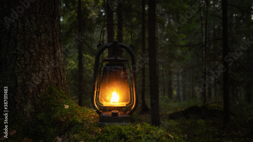 Old rusty oil lamp in dark autumn forest. Mystical scene with old kerosene lantern outdoor. Halloween concept.  photo