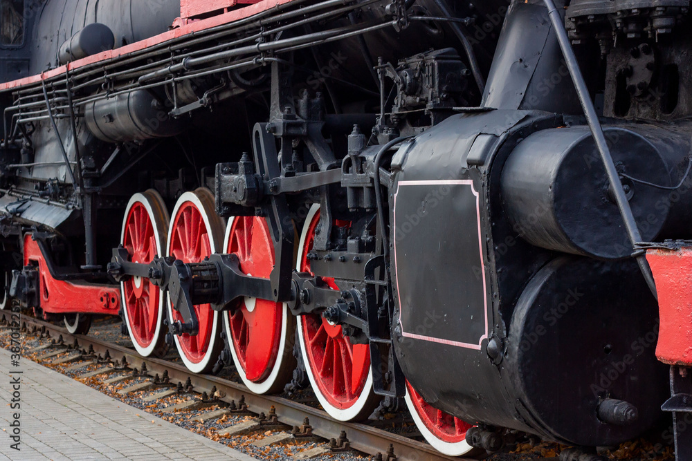 Old black and red retro steam locomotive wheels at the railway station. Vintage train staying on the railroad.