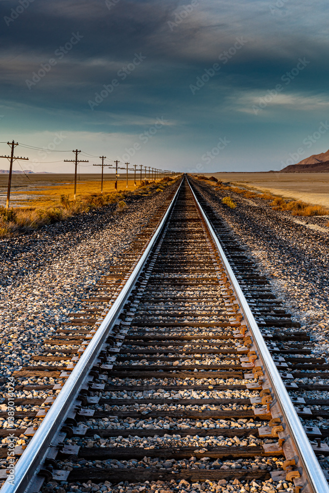 A nice landscape image of an old railroad track in the desert with a telegraph line next to it and mountains in the background. This beautiful image was taken during a gold hour sunset.