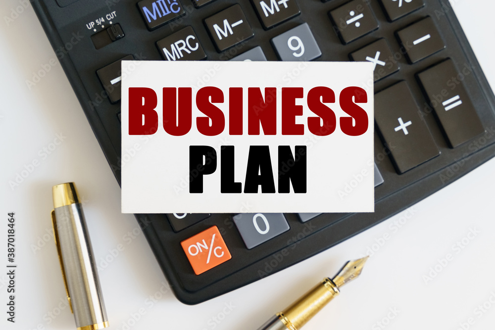 On the table there is a pen, a calculator and a business card on which the text is written - BUSINESS PLAN On the table there is a pen, a calculator and a business card on which the text is written - BUSINESS PLAN