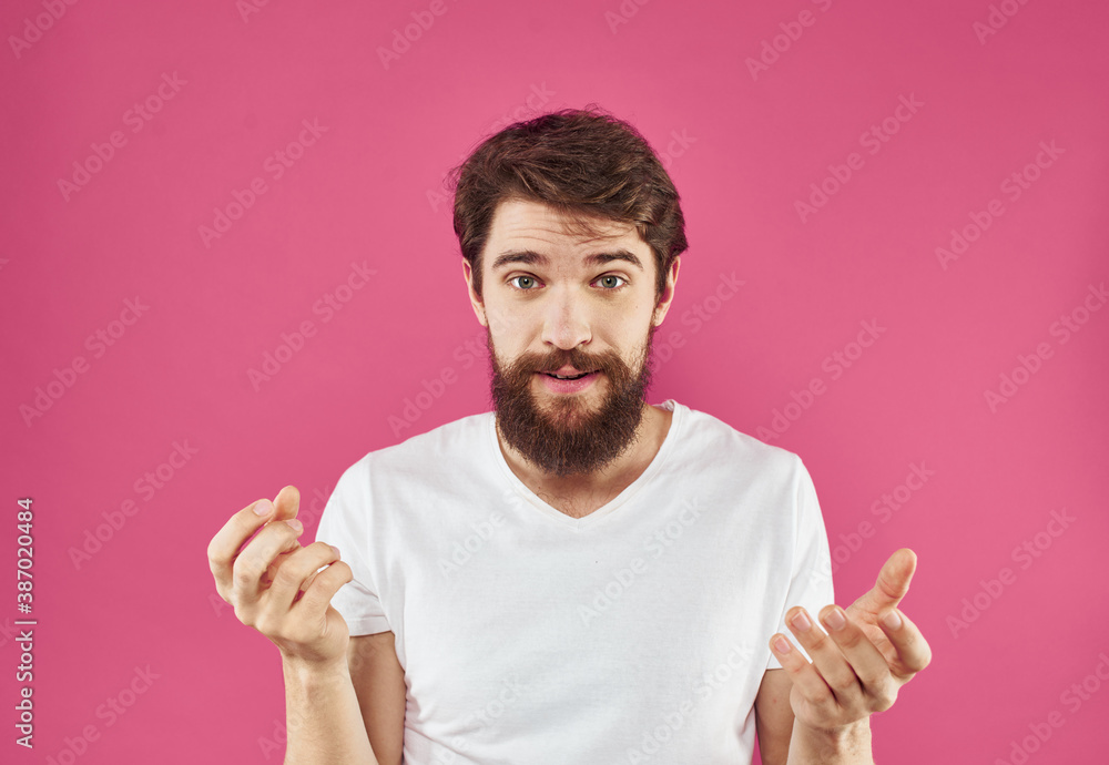 Happy young man on a pink background in a white T-shirt and a thick beard gesticulate with his hands Happy young man on a pink background in a white T-shirt and a thick beard gesticulate with his hands