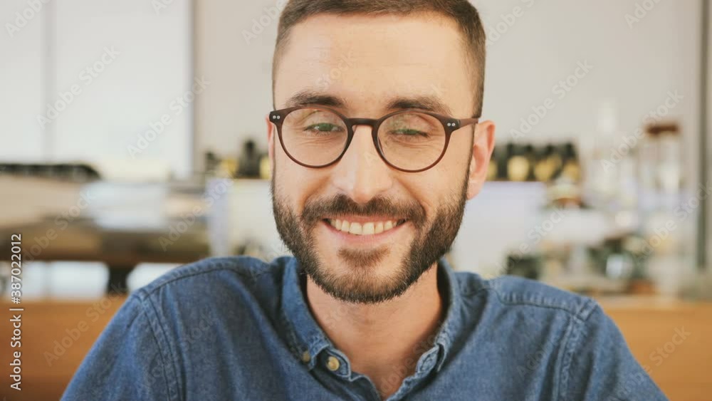 Close up portrait of young handsome caucasian man with beard and glasses. Cheerful guy sitting in cafe looking at camera and smiling. Close up portrait of young handsome caucasian man with beard and glasses. Cheerful guy sitting in cafe looking at camera and smiling.