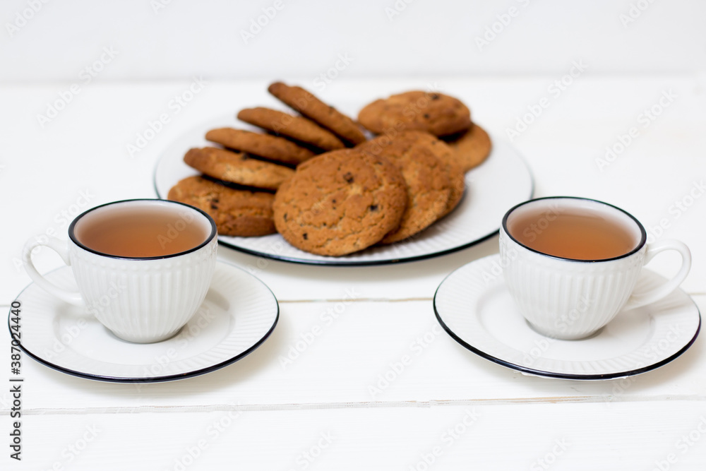 Two cups of tea and oatmeal cookies. Breakfast. Tea drinking. White wooden background. Two cups of tea and oatmeal cookies. Breakfast. Tea drinking. White wooden background.
