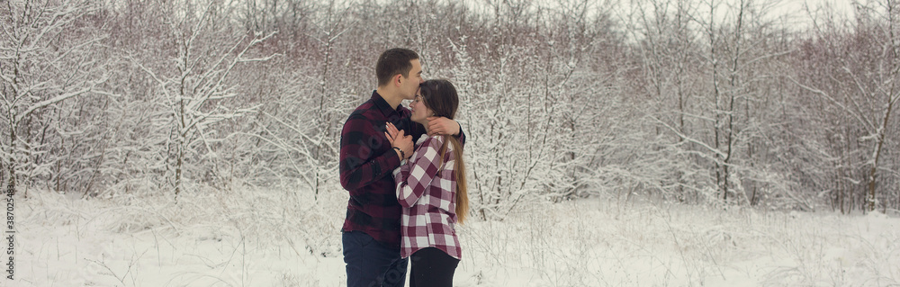 The guy and the girl have a rest in the winter woods. Husband and wife in the snow. Young couple walking in winter park The guy and the girl have a rest in the winter woods. Husband and wife in the snow. Young couple walking in winter park