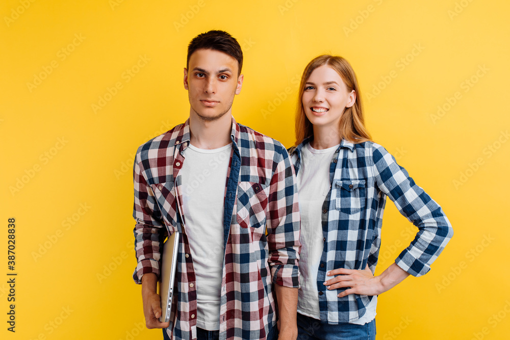 Beautiful young couple of students, man and woman with laptop on yellow background Beautiful young couple of students, man and woman with laptop on yellow background