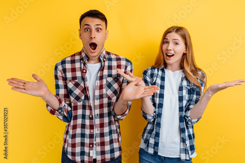 Shocked excited young couple  man and woman in plaid shirt  on yellow background