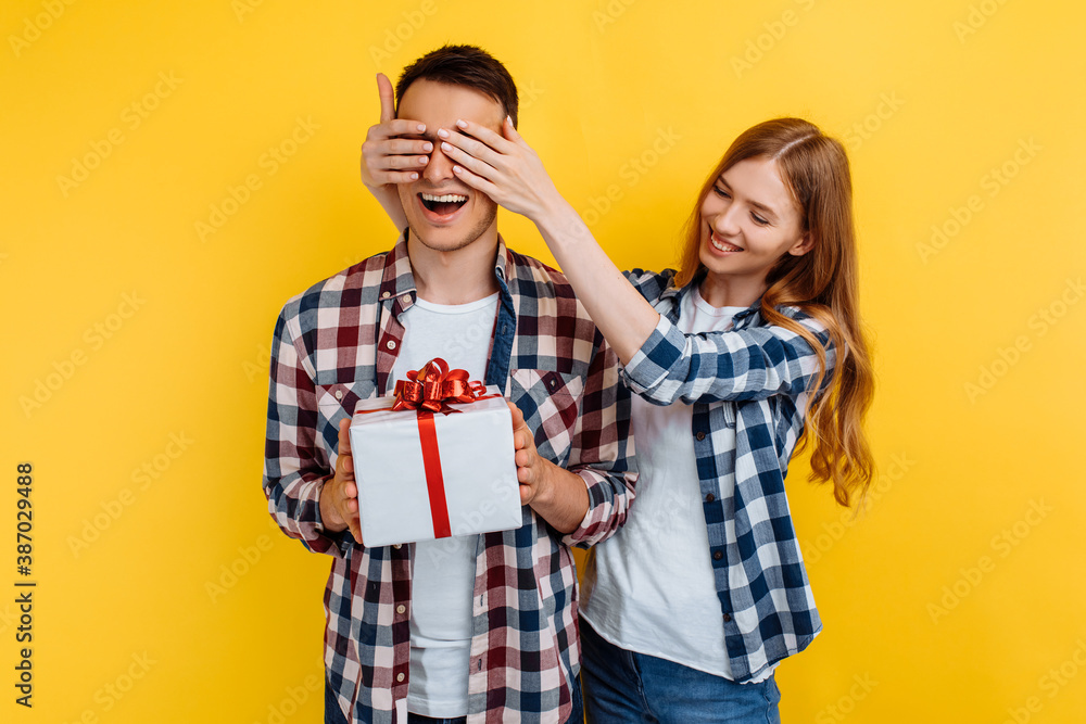 Happy young couple in love, woman makes a surprise, gives a gift to a man on a yellow background, Valentine's Day Happy young couple in love, woman makes a surprise, gives a gift to a man on a yellow background, Valentine's Day