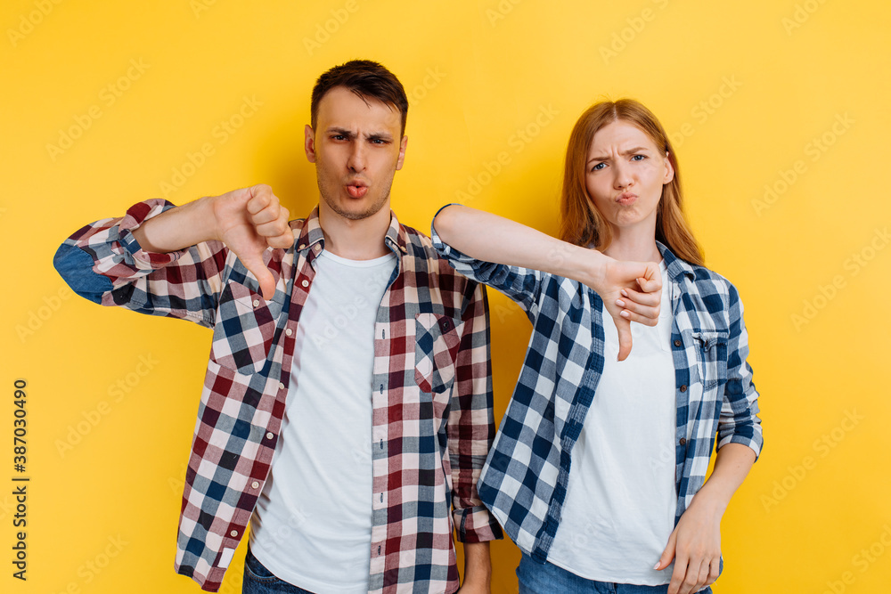 Young couple, man and woman showing dislike gesture on yellow background Young couple, man and woman showing dislike gesture on yellow background