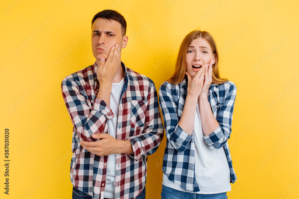 Young couple, man and woman suffering from toothache, holding on to the cheek, on yellow background Young couple, man and woman suffering from toothache, holding on to the cheek, on yellow background