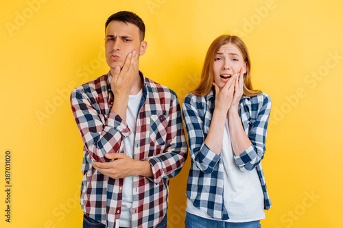 Young couple, man and woman suffering from toothache, holding on to the cheek, on yellow background